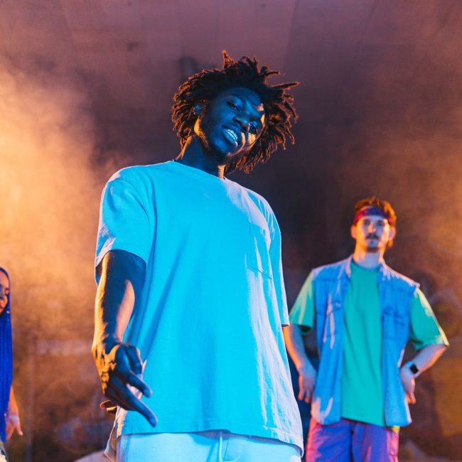 Vibrant group of friends performing on stage with dynamic lighting and smoke effects.